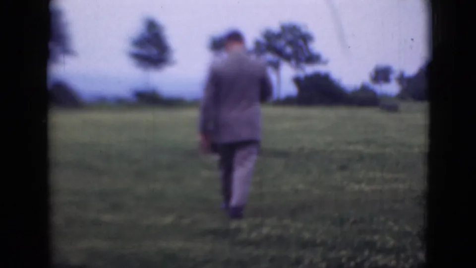 In 1947 Middletown, Pennsylvania footage, a man in a grey suit and hat walks away across open grass with trees in the distance.
