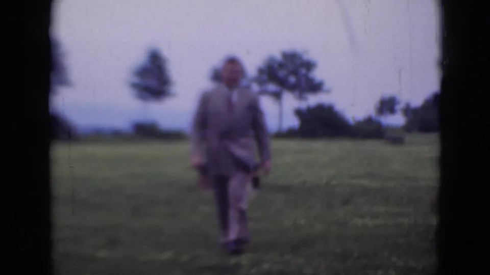 A suited adult man walks through open grass in Middletown, Pennsylvania, in archival 8mm footage dated 1947.