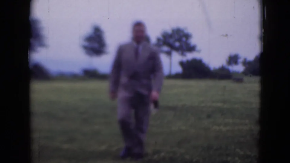 The man remains in the open field, framed softly against grass, trees, and a pale sky in 1947 home-movie footage.