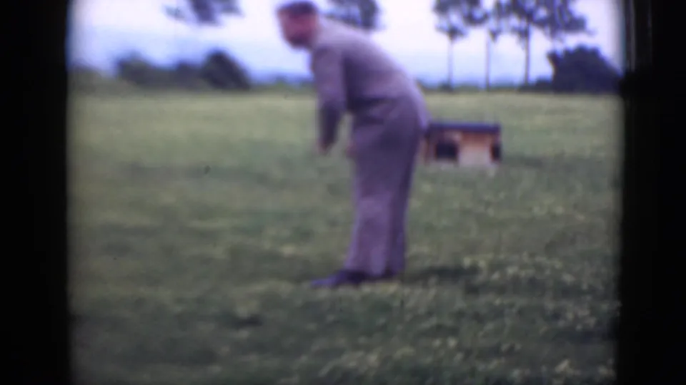 The suited man stays bent over in the Pennsylvania field, appearing to reach toward the ground near patches of clover.