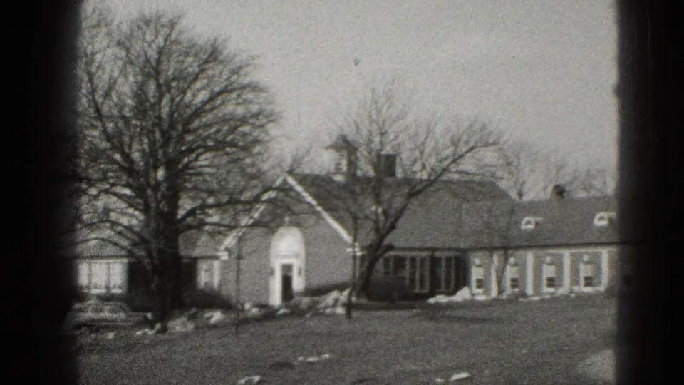 Middletown residential building with an arched doorway, dormer windows, bare trees, and open lawn in black-and-white 8mm footage.
