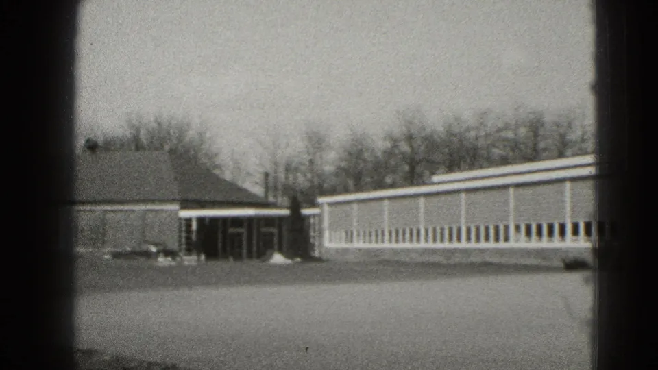 Middletown 8mm frame showing connected low buildings, a covered doorway, long windowed wing, lawn, and bare trees.