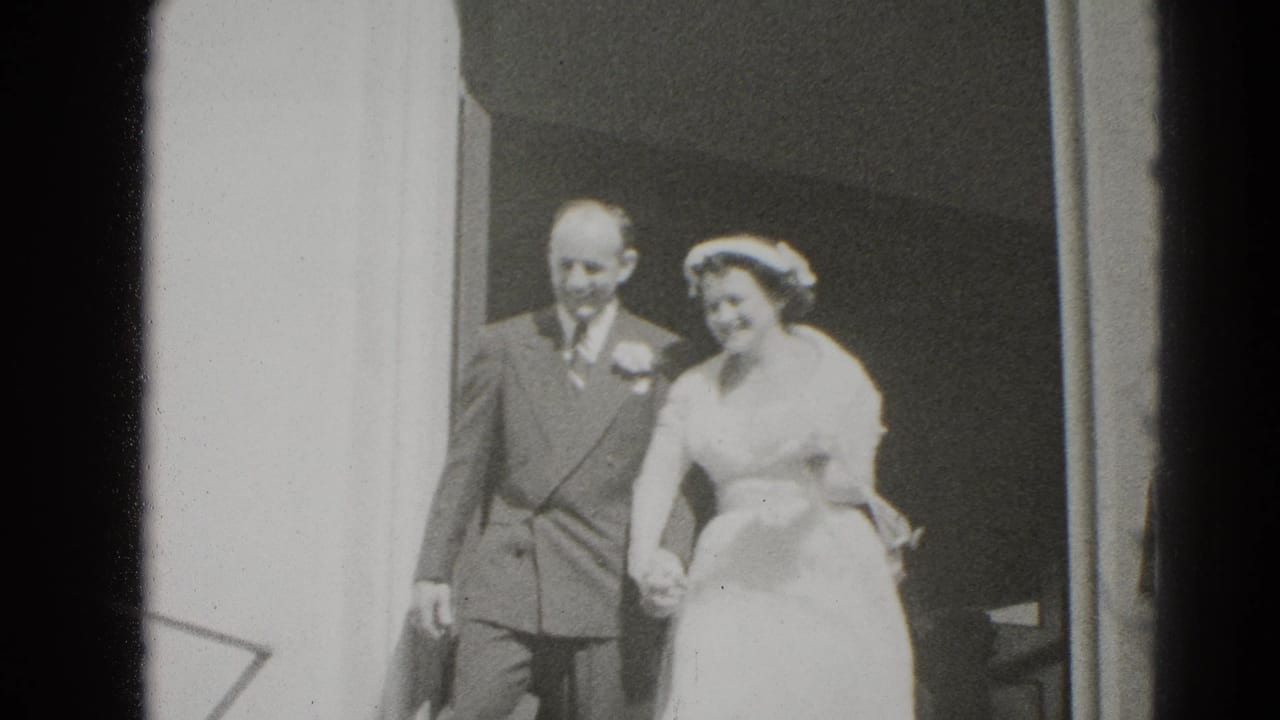 Bride and groom step out together from a doorway, holding hands and smiling.