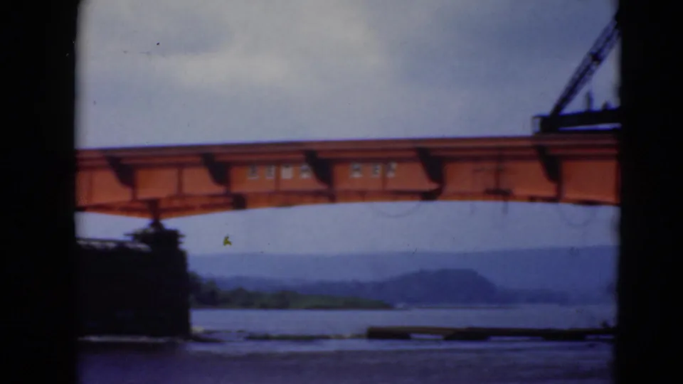 8mm view of the orange bridge span over the river, with distant hills and a crane boom entering near the upper right.