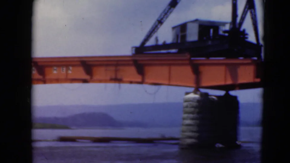 1940s 8mm view of an orange crane structure and steel beam above water near Middletown, Pennsylvania, with hills in the distance.