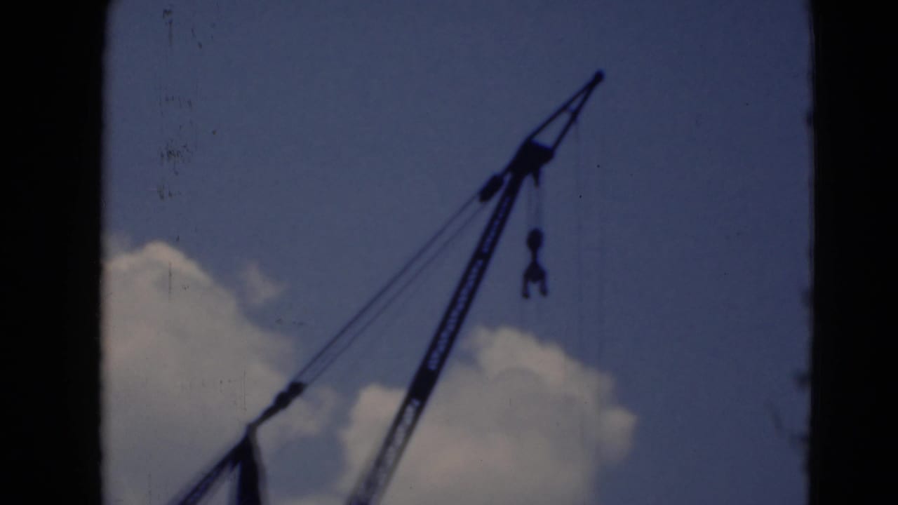 Silhouetted crane boom against a cloudy blue sky.