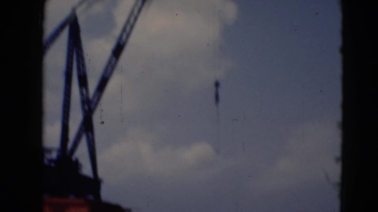 A closer view of a crane frame and suspended hook appears in soft 8mm color near the riverfront.