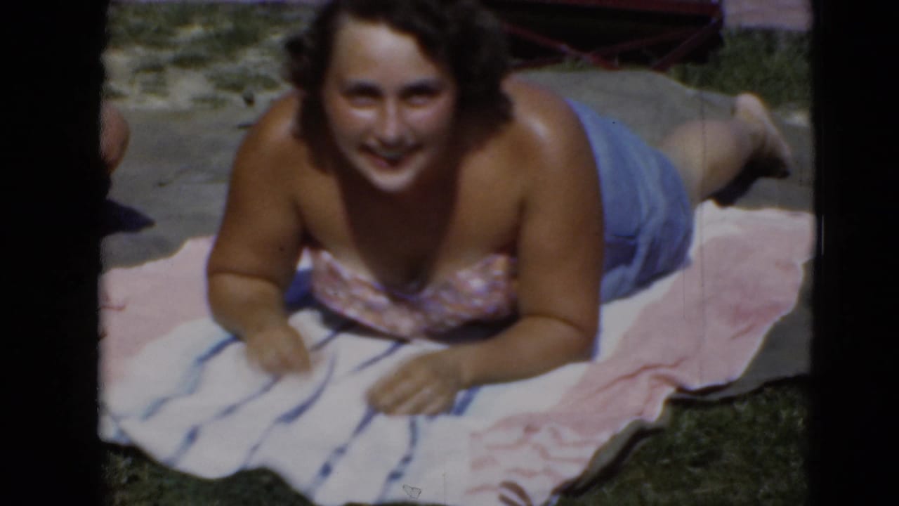 Woman sunbathing on striped and pink towels in a grassy Middletown, Pennsylvania yard in archival 8mm footage.