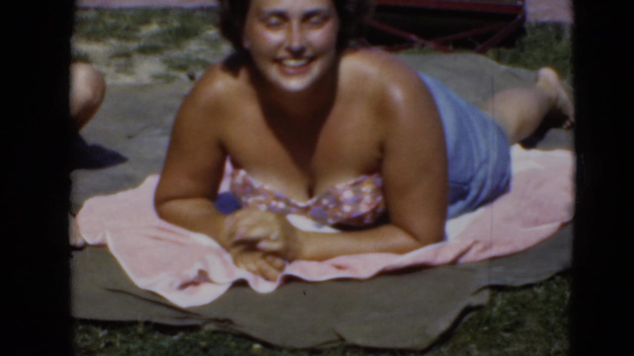 Woman in a floral swimsuit lying on towels outdoors and facing the camera.