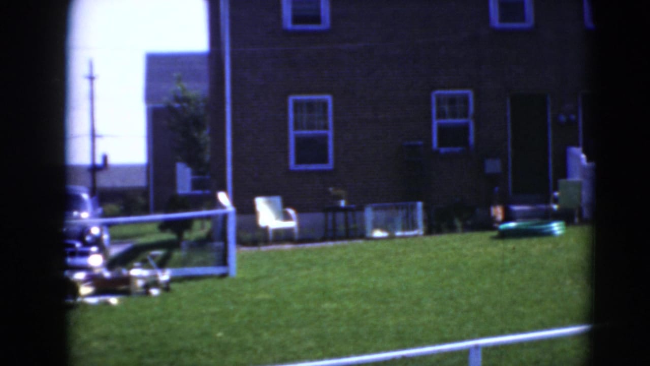 Brick house and green lawn with a white chair, parked car, railing, and toy vehicle.