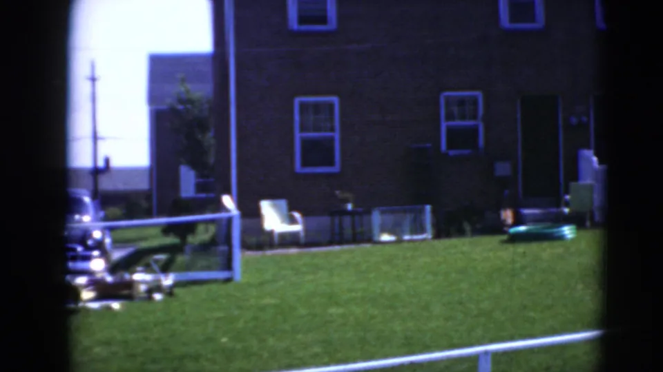 Middletown, Pennsylvania home-movie frame showing a brick house, green yard, white lawn chair, parked car, and small toy vehicle.