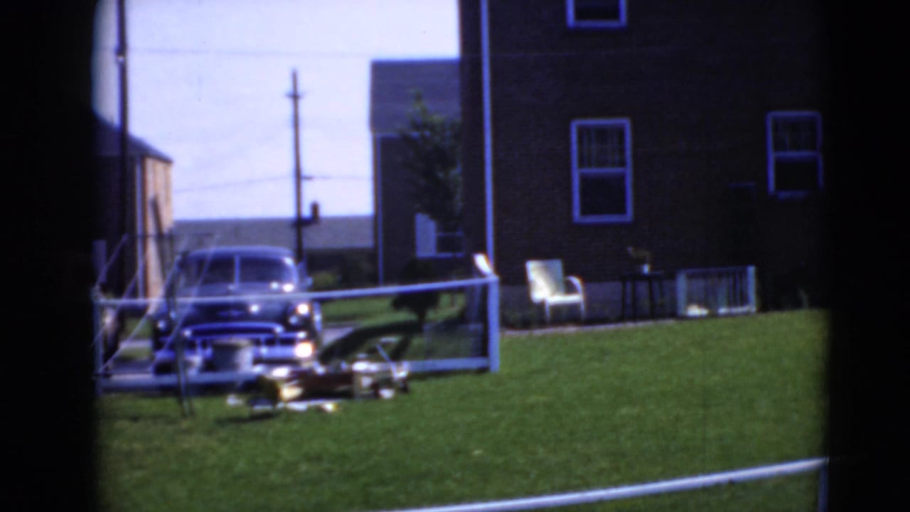 Parked car beside a brick house with a lawn chair, green grass, and window-frame edges.