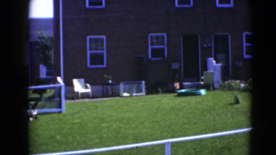 Middletown residential yard view showing a brick house, white-trim windows, green lawn, low railing, and a white lawn chair.