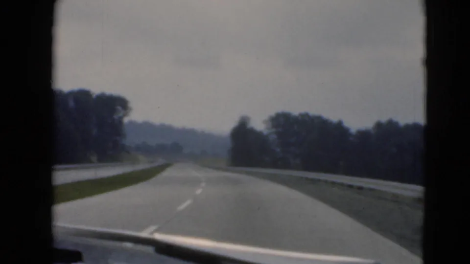 A forward road view shows a paved lane, roadside guardrail, wooded edges, and hazy Pennsylvania hills ahead.