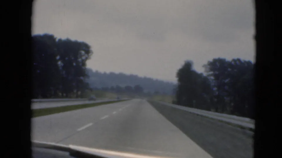 Forward-facing in-car view of a Pennsylvania divided highway, showing guardrails, sparse traffic, trees, and muted overcast light.