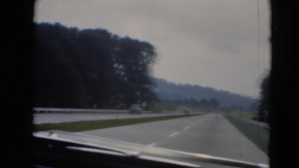 In-car home-movie view along a divided highway near Middletown, with the car hood visible, trees lining the road, and another vehicle ahead.