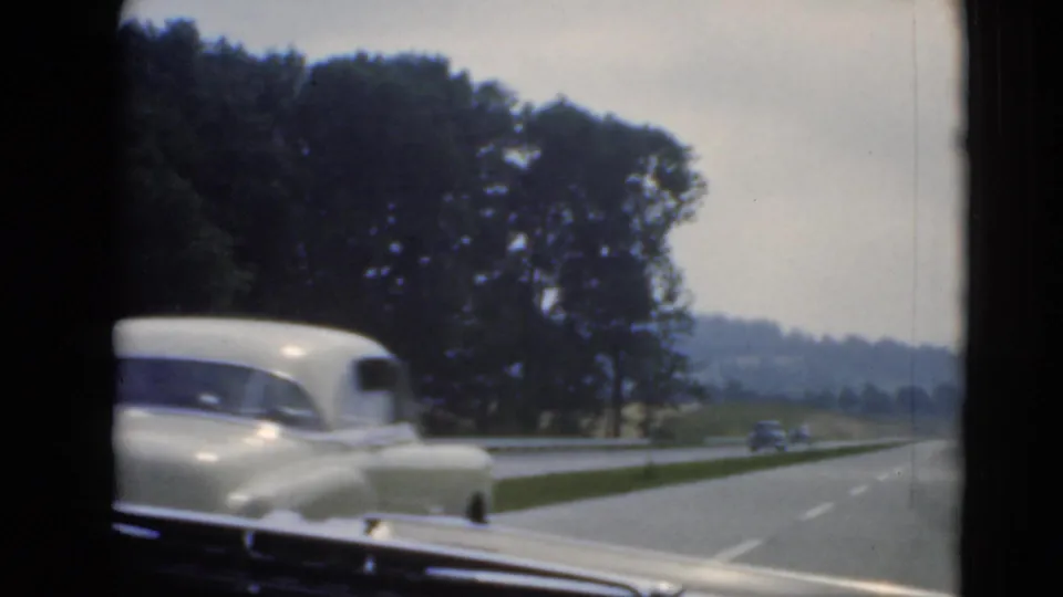 Driver's-side view of a light-colored vintage sedan on a divided roadway near Middletown, Pennsylvania, with trees and low hills beyond.