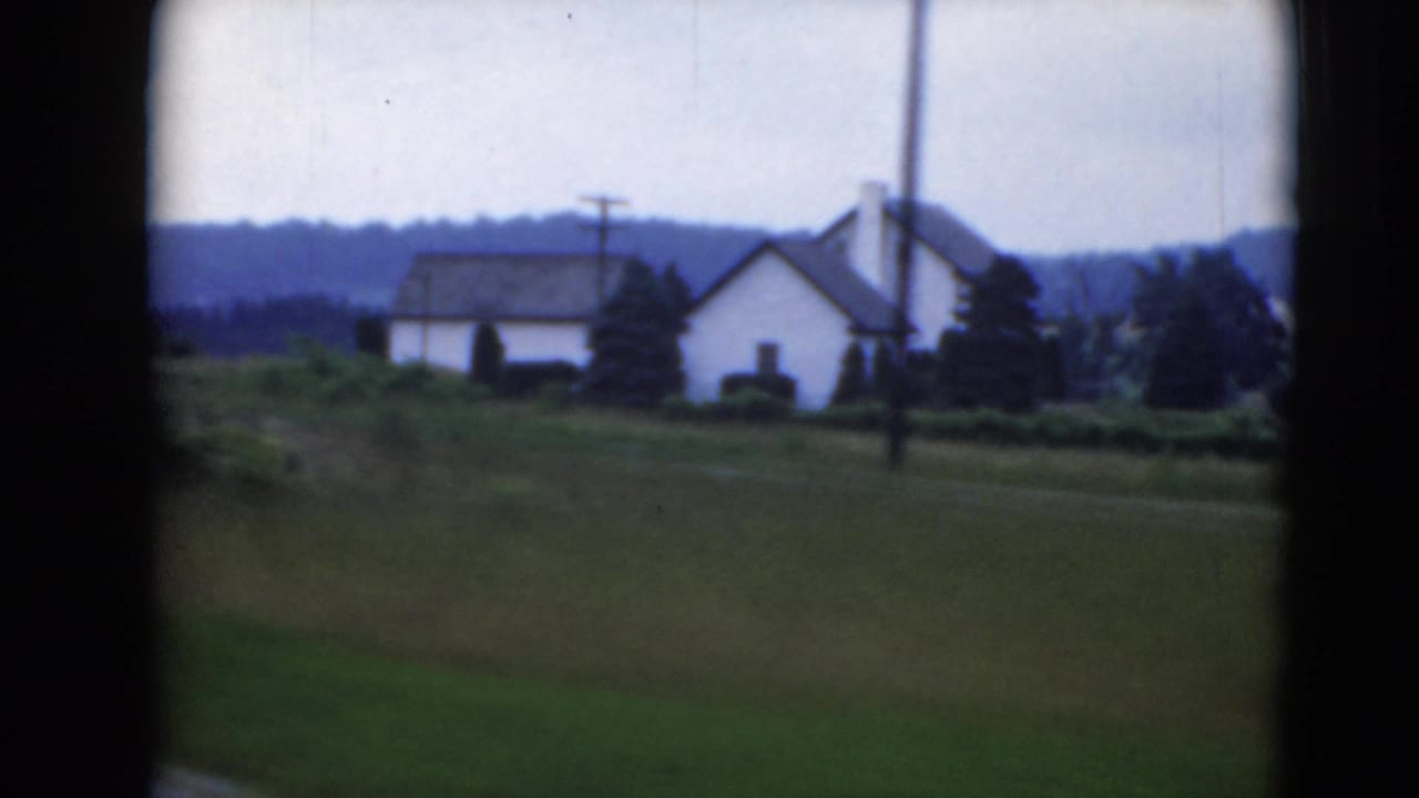 White rural houses and green fields seen from a moving vehicle.
