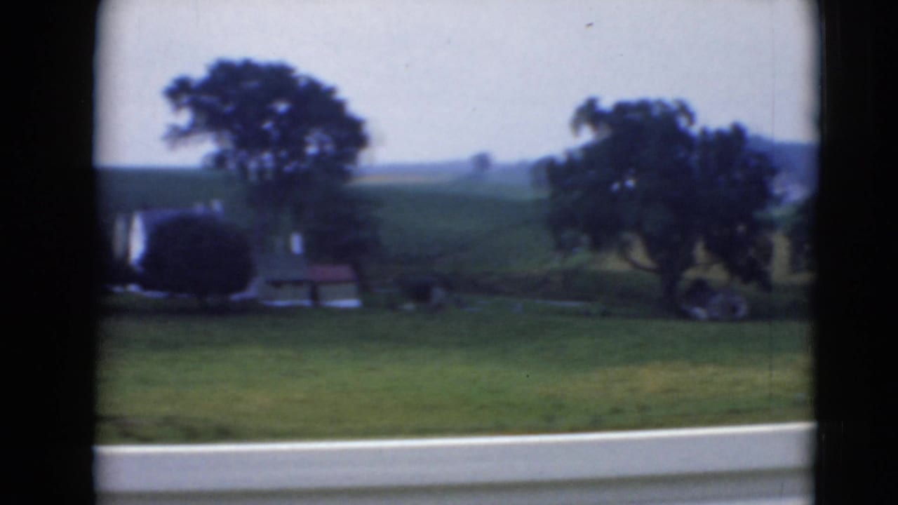 Rural Middletown, Pennsylvania landscape with green hills, trees, small structures, and a road edge seen through dark window framing.