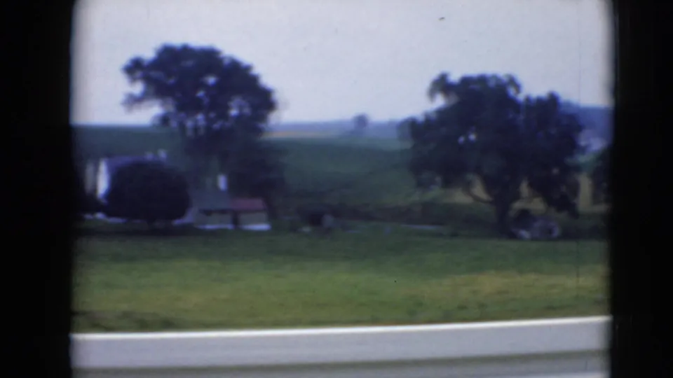 Rural Middletown, Pennsylvania landscape with green hills, trees, small structures, and a road edge seen through dark window framing.