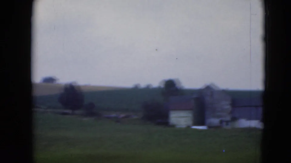 Soft 8mm view of rural Middletown fields with a small building, trees, and a white structure across rolling ground.