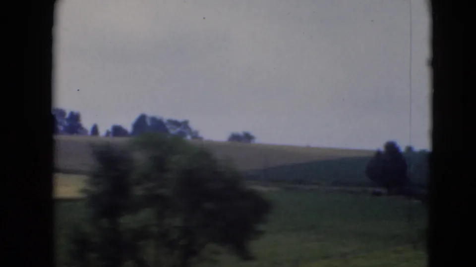 Rural Pennsylvania fields and distant tree line with foreground motion blur, filmed in soft 8mm color.