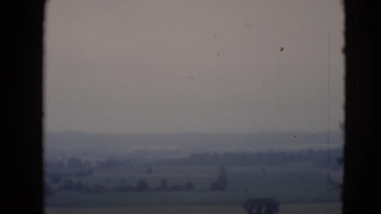 Rolling fields and distant trees framed by dark vertical window edges.
