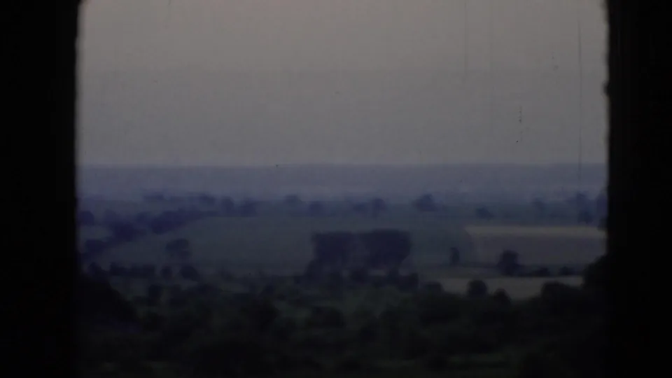 A soft 8mm view from a moving vehicle shows Pennsylvania fields, scattered trees, and a hazy horizon.