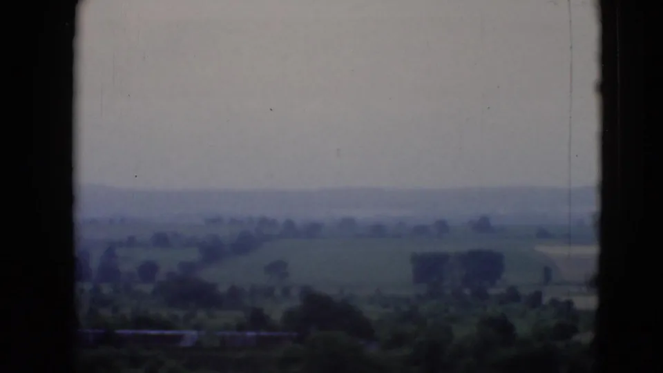 The final frame shows rural Pennsylvania fields and tree clusters through dark vehicle-window framing on grainy 8mm film.