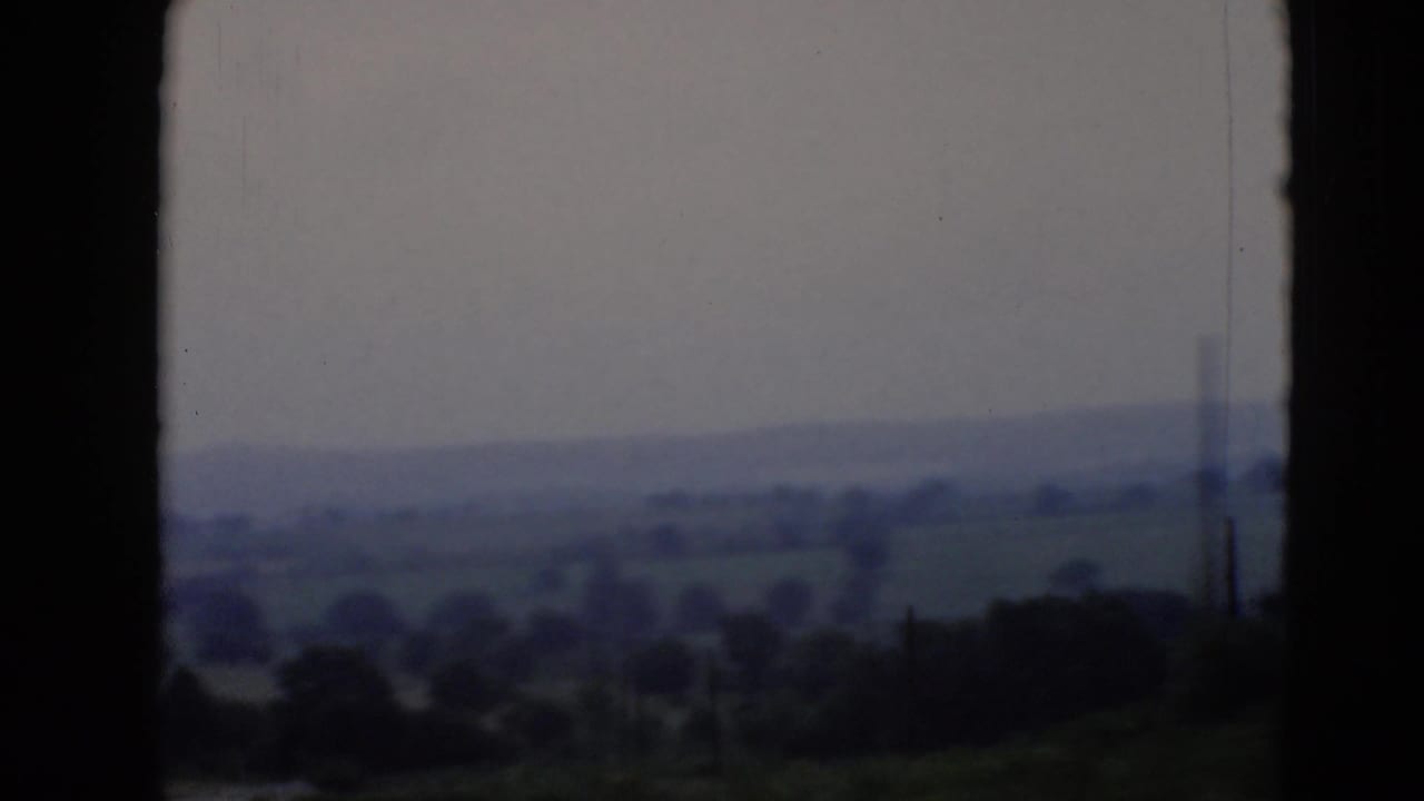 Distant hills and fields framed by the silhouette of a plane window.