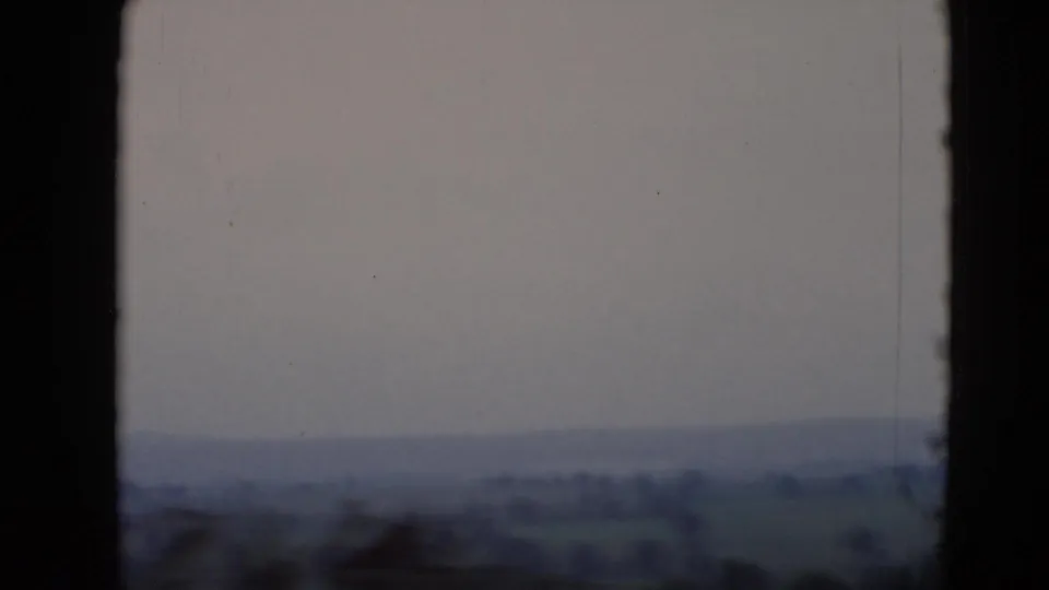 The frame shows a soft-focus 8mm view of rural terrain from an aircraft, with dark window borders and hazy Pennsylvania hills.
