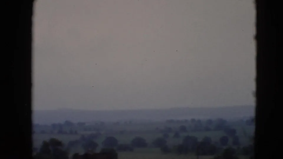 A 1940s home-movie frame looks through a plane window toward green fields, scattered trees, and distant hills near Middletown, Pennsylvania.