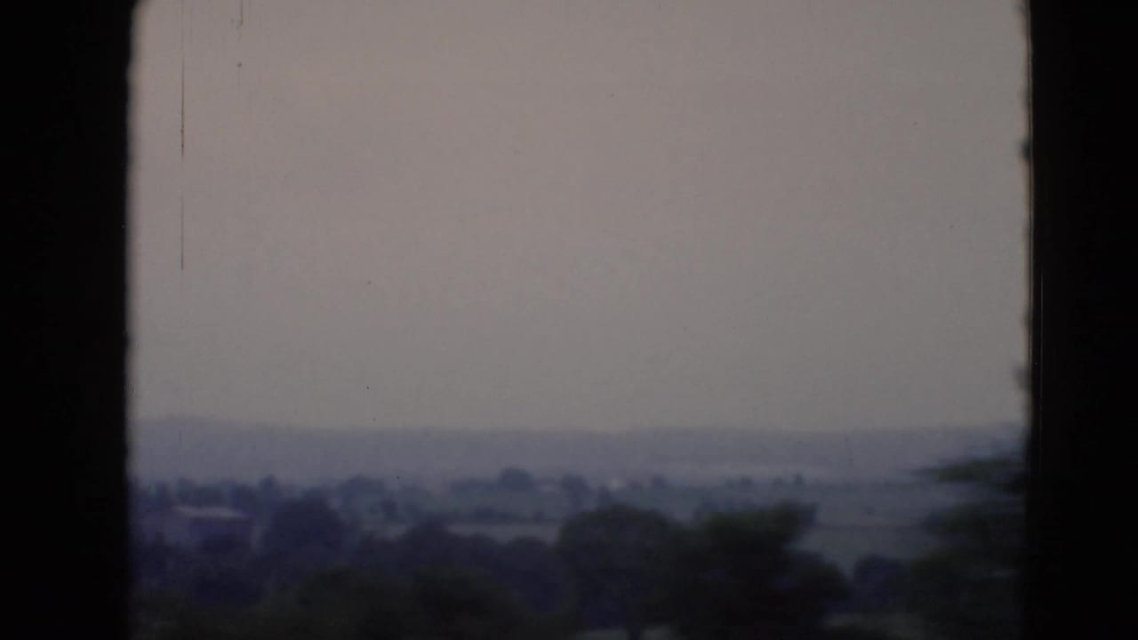 Window-framed view of distant fields and trees under a gray sky.