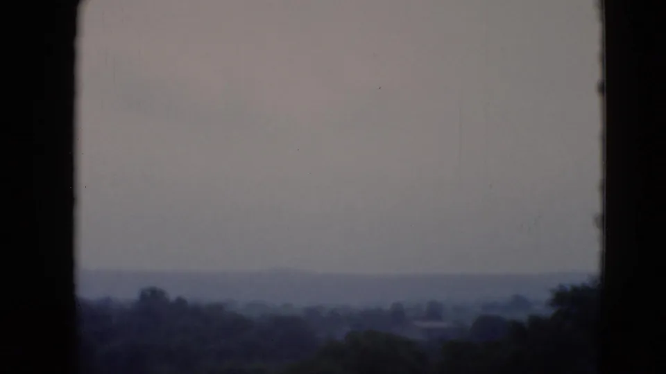 1947 home-movie view near Middletown, Pennsylvania, with dark window edges around a hazy field and tree-lined horizon.
