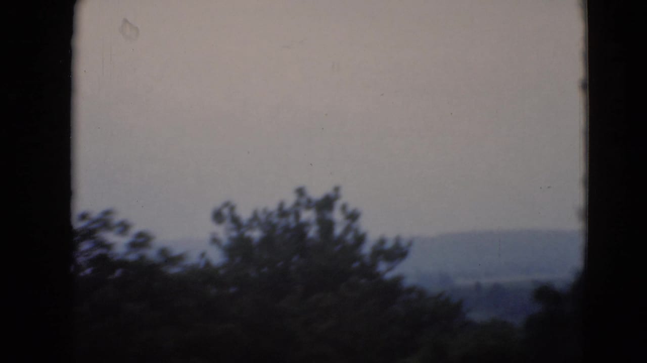 Hazy rural hills and treelines viewed through a dark window frame in archival home-movie footage associated with Middletown, Pennsylvania.
