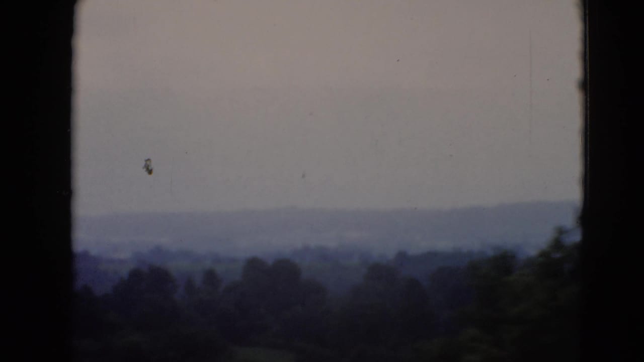 Distant wooded hills under a pale sky, divided by a window frame.