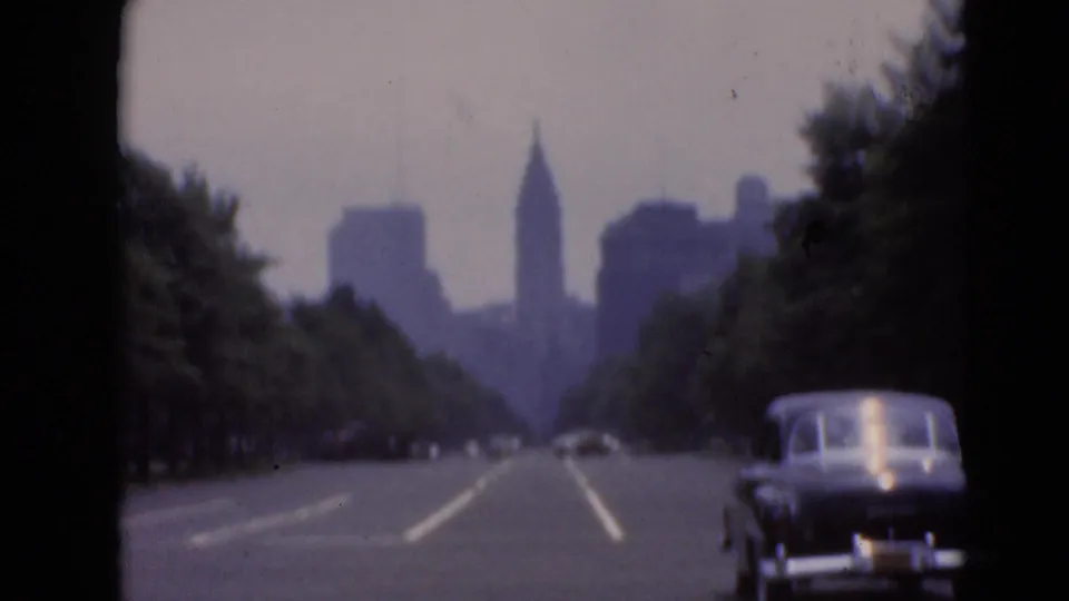 Vintage road scene with mid-century cars and a soft distant skyline, including a prominent pointed spire.