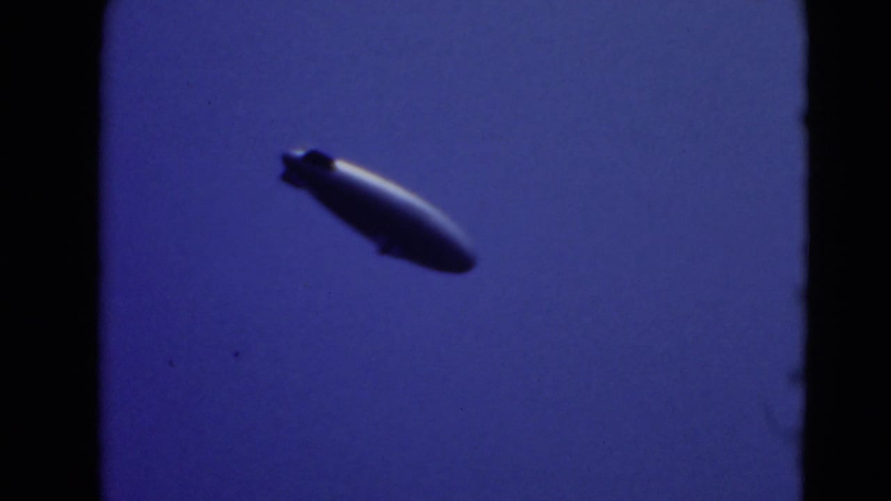Dark blimp silhouette floating against a blue sky.