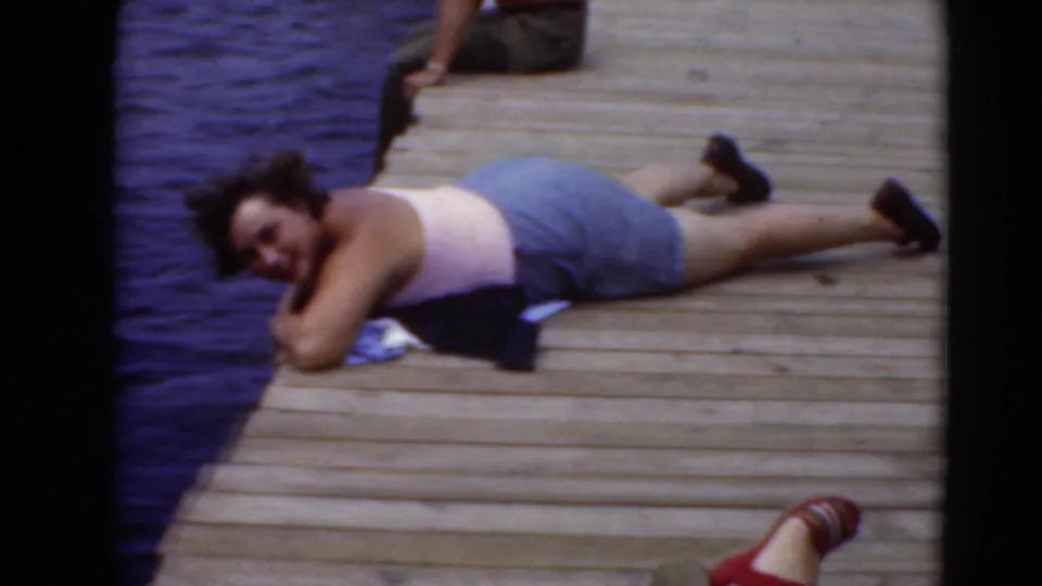 An adult on a Middletown dock turns toward the home-movie camera while resting near blue water.