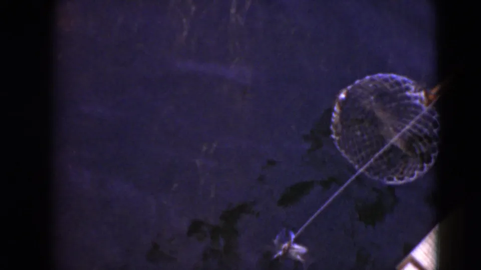 1940s 8mm home-movie frame showing a circular dip net on a pole in dark water, likely during crab fishing near Middletown, Pennsylvania.