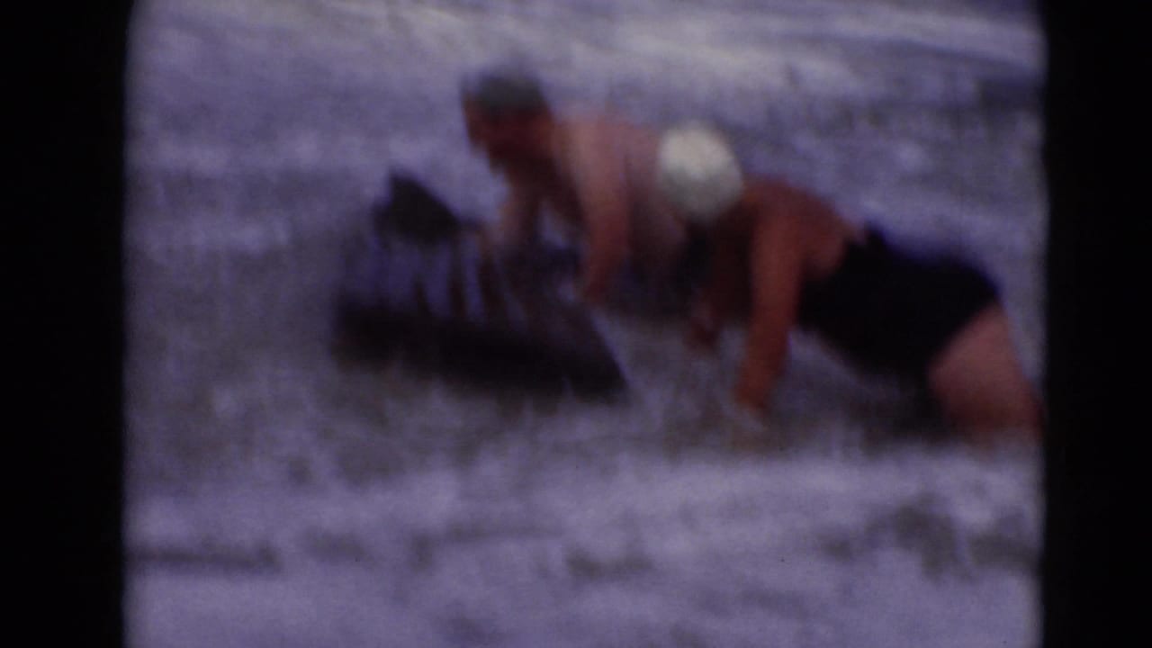 A woman in a white swim cap leans over a dark float in foamy water.