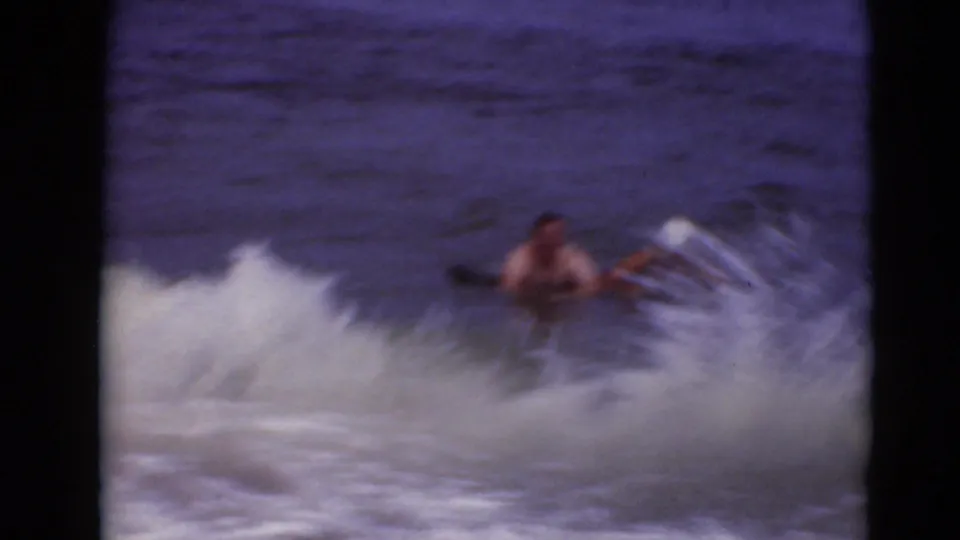 The riders appear partly separated from the float as surf breaks around them near the shoreline.