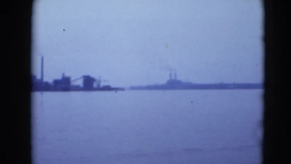 1940s 8mm view of a hazy Middletown, Pennsylvania waterfront with low industrial structures across calm water.