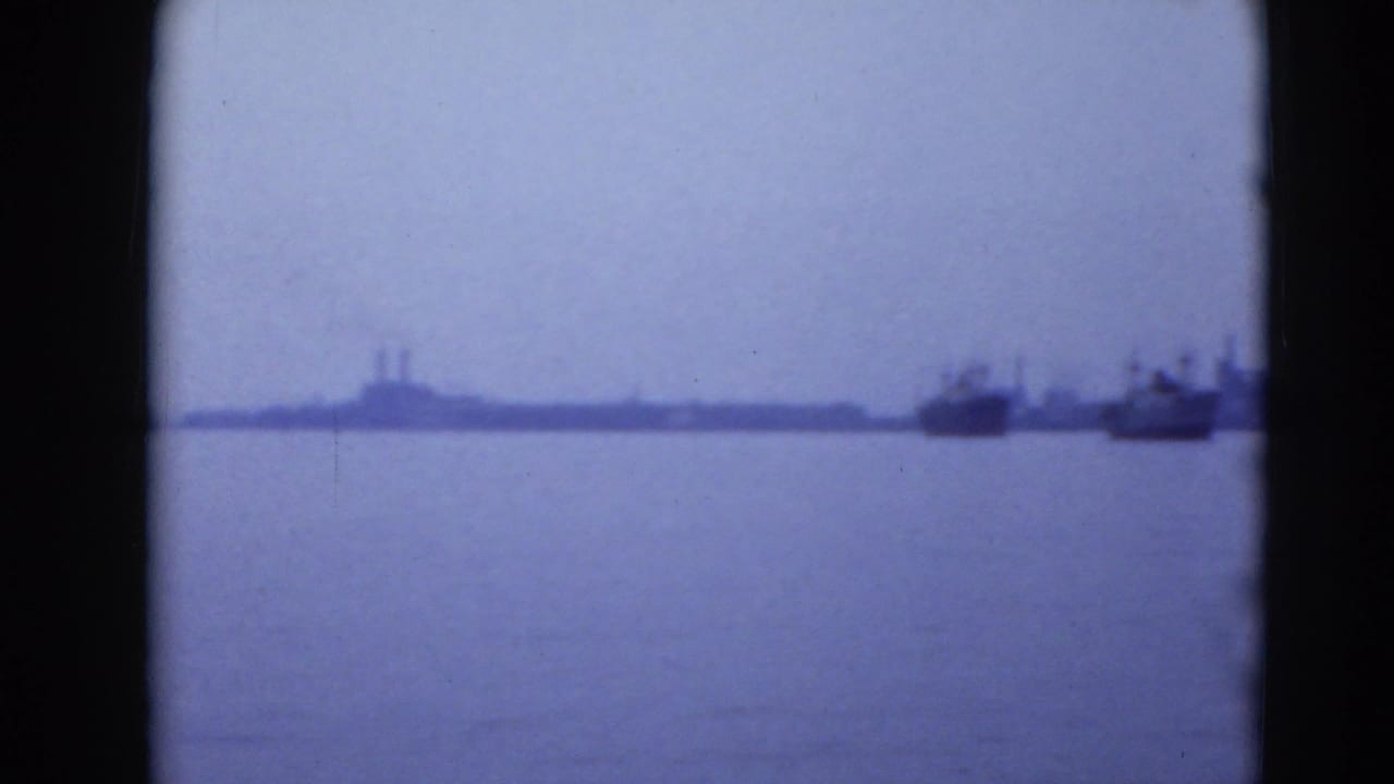 Hazy shoreline with boats at the right edge across open water.