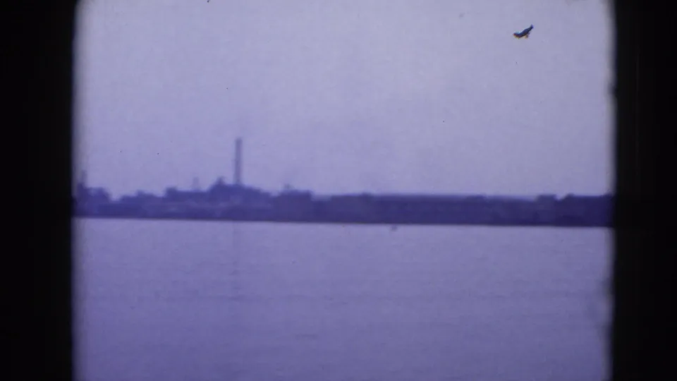 Hazy 8mm view of the Middletown waterfront, with a smokestack and low shoreline beyond broad open water.