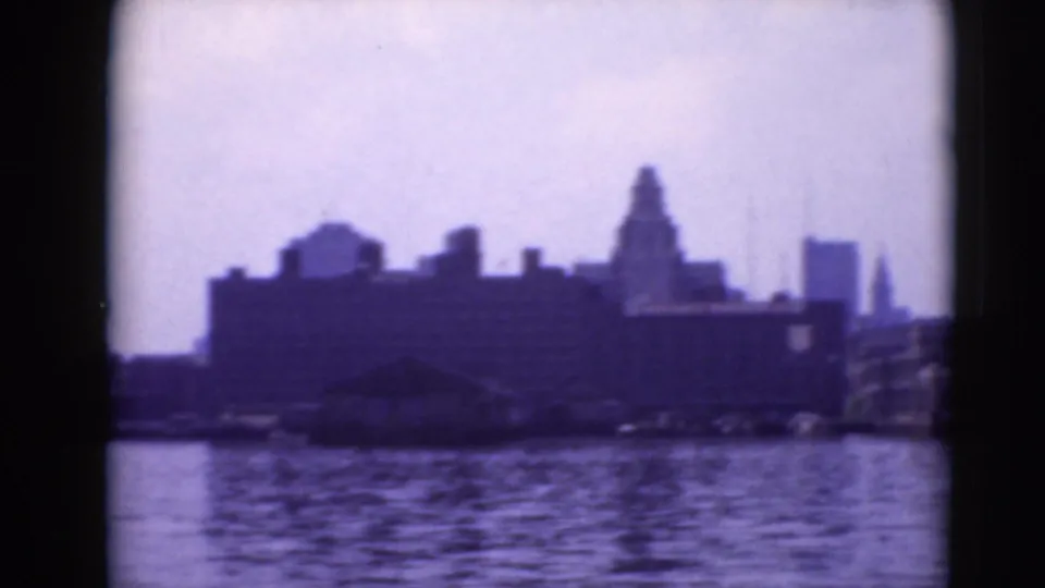 Blue-purple 8mm frame looking across water toward a Pennsylvania waterfront with dark building silhouettes and soft skyline forms.