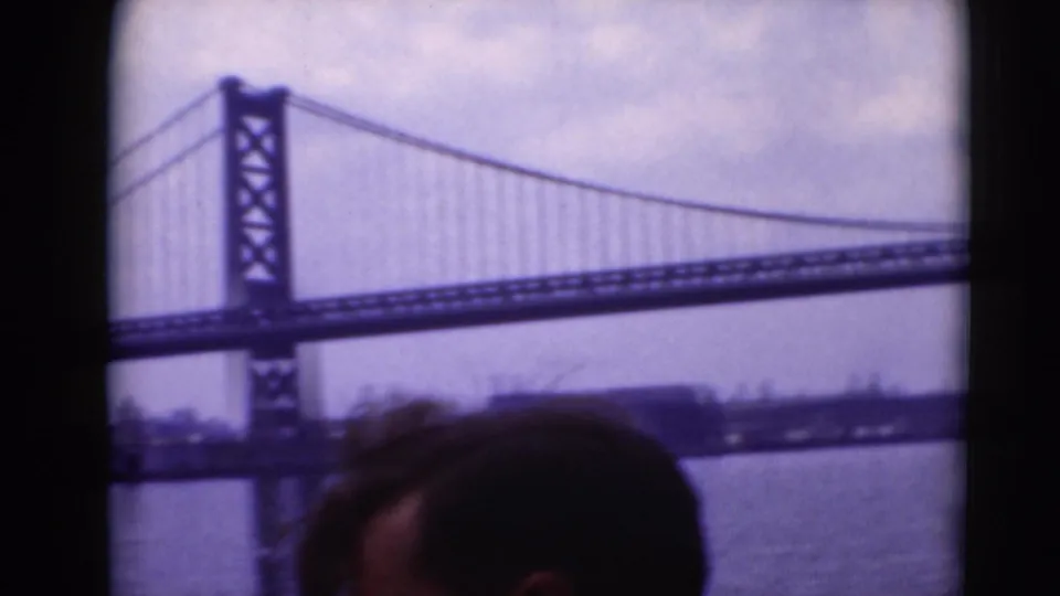 A suspension bridge tower and cables dominate the river view, with a partial passenger head visible along the lower edge.