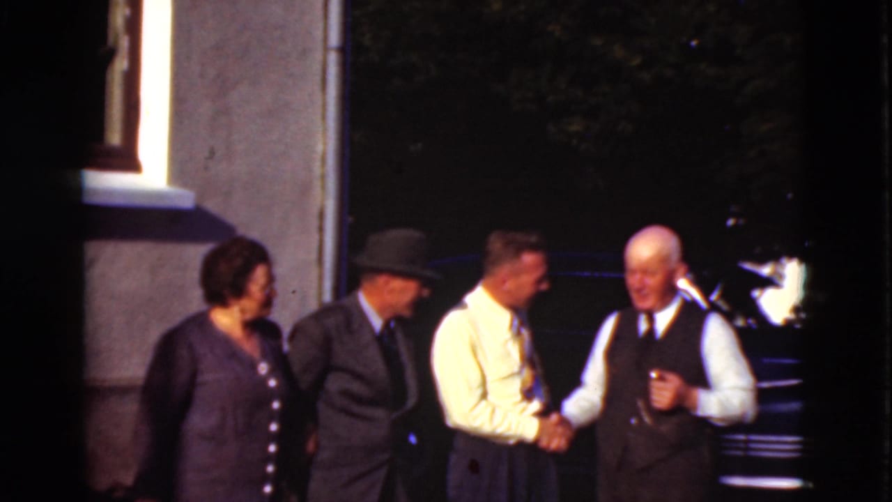 The Denmark 1975 frame shows a friendly handshake among adults, with a woman, a suited man in a hat, and a dark car behind them.