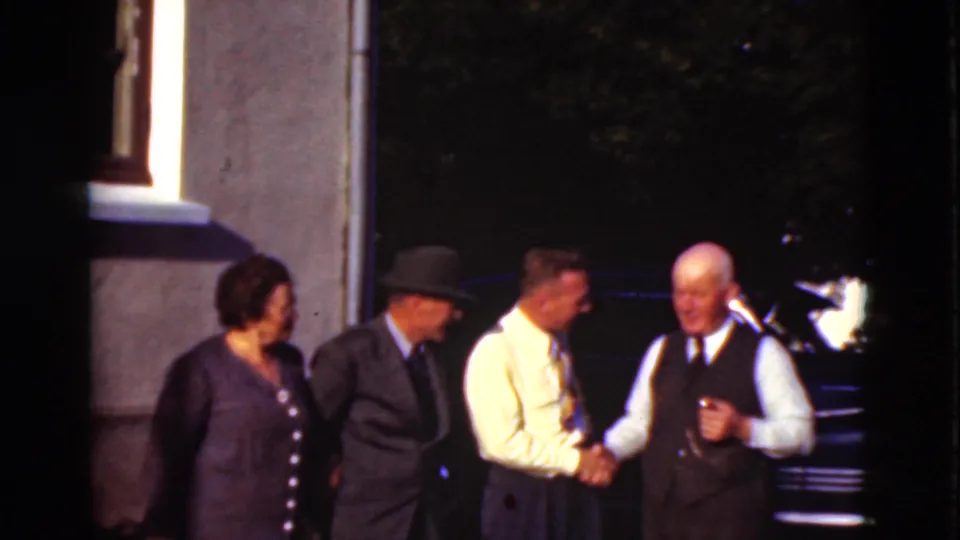 The Denmark 1975 frame shows a friendly handshake among adults, with a woman, a suited man in a hat, and a dark car behind them.