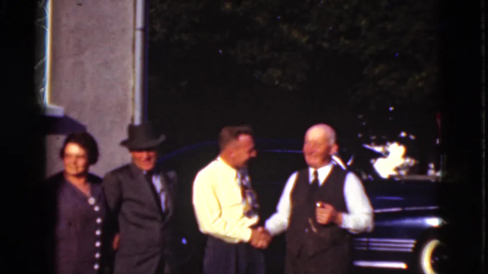 In this 1975 Denmark home-movie still, the group remains clustered outside as two men shake hands and the others watch nearby.